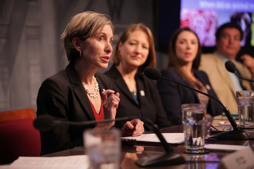 Beth Allgood sitting at a large table speaking in front of other people